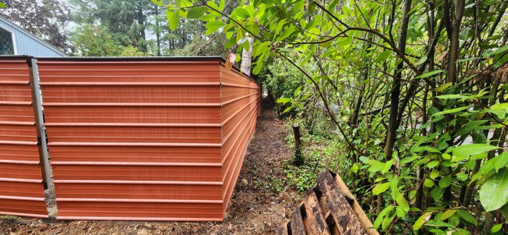 finished fence, concrete footing, galvanized steel posts, pressure treated stringers, metal panels, with a Trex deck board cap.